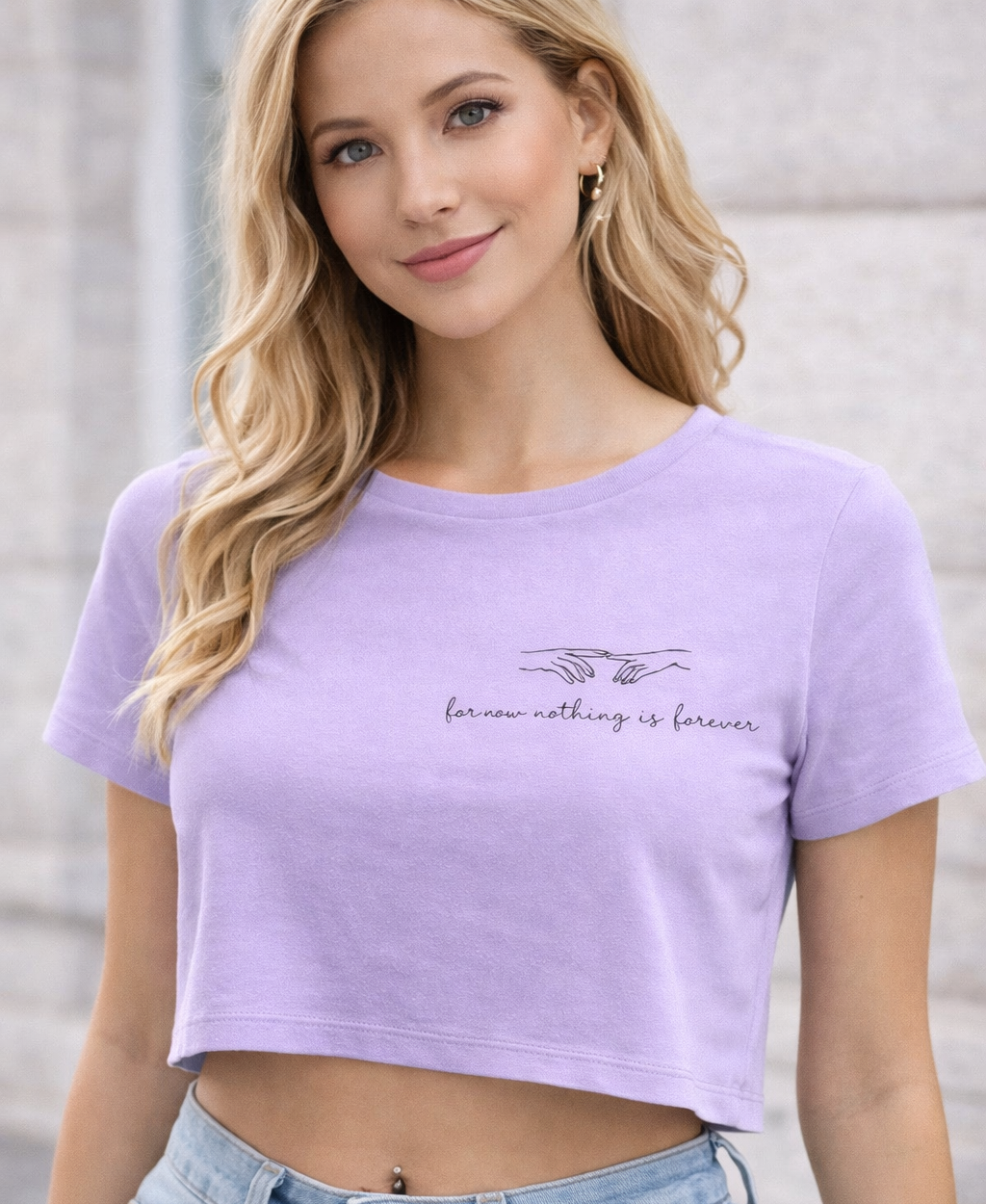 Woman wearing a purple crop top with text and light blue jeans against a neutral background